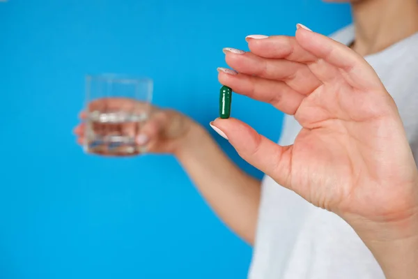 The medicine. The woman takes a pill. Tablet and glass of water in female hands on a blue background. Health care and people concept