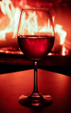 Yanan bir şöminenin arka ışığında bir kadeh beyaz şarabın yakın çekimi..
