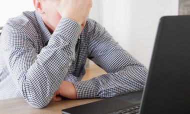 Uzaktan bilgisayarla çalışmaktan yorulan adam masaya yaslandı ve eliyle yüzünü kapattı..