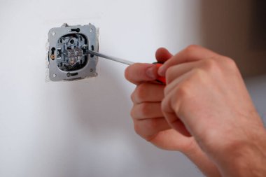 Elektrikçi anahtarı tornavidayla söker. Ellere yakın çekim. Bir elektrikçinin rutin işi. Bağlantıları kontrol ediyorum. Değiştir.