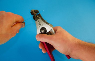 Profesyonel aletli erkek eller bakır teldeki yalıtımı kaldırır. Striptizci yakın plan iş yapar. Elektrik mühendisliği kavramı.