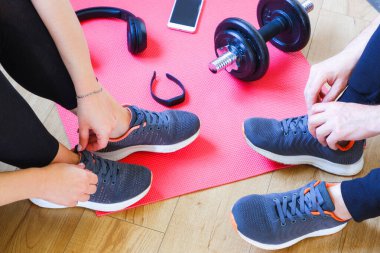 Ev antrenmanı. Tanınmayan bir erkek ve kadın, dambıl egzersizinden sonra koşmaktan gurur duyar. Kulaklıklar, spor bileziği ve halterler paspasın üzerinde..