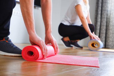 Ev antrenmanı. Tanınmayan bir kadın ve spor giysili bir erkek evde antrenman yapacaklar. Paspasları spor olsun diye gevşeten insanların ellerine bakın..