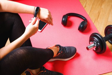 Ev antrenmanı. Tanınmayan bir kadın, bir dambıl egzersizinden sonra koşmaktan gurur duyar. Kulaklıklar, spor bileziği ve halterler paspasın üzerinde..
