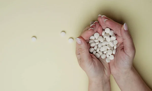 Female palms hold pills against yellow background. A handful of white pills in hands. Medicine, healthcare concept