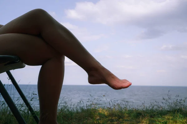 Rest in the forest by the river. A woman relaxes on a sun lounger on a large large river. Backlit leg view.