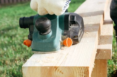 Bir müteahhit yeni bir evin inşaatında bir pano tasarlıyor. Eldivenli ellerde elektrikli bir uçakla yakın plan..