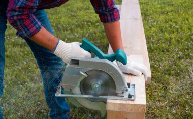 Elektrikli el testereli bir adam çimenlikte tahta testeresi kullanıyor. ÇEVİR.