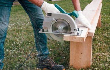 Elektrikli el testereli bir adam çimenlikte tahta testeresi kullanıyor. ÇEVİR.