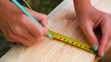 Kadın marangoz tahta bir tahtada kalem izi yapar. ÇEVİR.