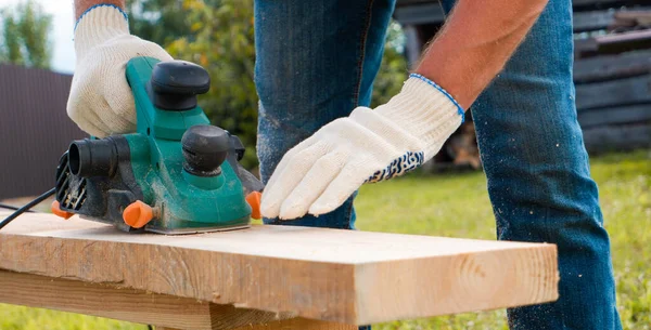 Bir müteahhit yeni bir evin inşaatında bir pano tasarlıyor. Eldivenli ellerde elektrikli bir uçakla yakın plan..