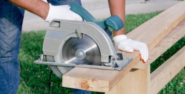 Bir erkek katılımcı el testeresi ile çalışır. İnşaatçının biri bir evin inşaat alanında tahta kesiyor..