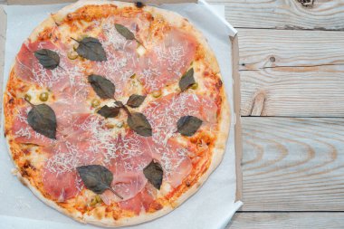 Prosciutto etli pizza yakın plan. Kaba ahşap bir masanın üstünde peynirli ve fesleğenli etli pizza. Metnin için yer.