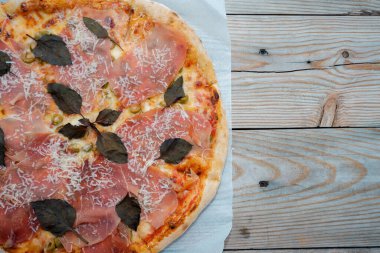 Prosciutto etli pizza yakın plan. Kaba ahşap bir masanın üstünde peynirli ve fesleğenli etli pizza. Metnin için yer.