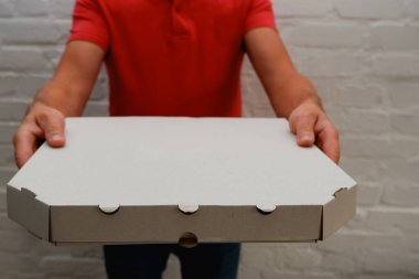Pizza teslimatı Kırmızı polo giyen bir kurye, içinde pizza olan bir karton kutu tutuyor. Yemek teslimatı