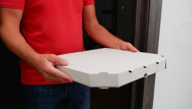 Pizza teslimatı Kırmızı polo giyen bir kurye, içinde pizza olan bir karton kutu tutuyor. Yemek teslimatı