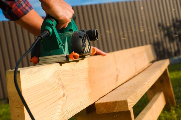 A carpenter planes a wooden board with an electric plane. Planing wooden plank with a electric plane.