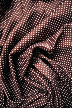 Beyaz noktalı ve zarif kıvrımlı kahverengi kumaş. Tekstil dokusu, moda projeleri, tasarım, dikiş ve reklamlar için arka plan olarak mükemmel bir retro ve stil ortamı yaratır..