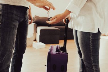 Evin anahtarlarını tutan bir adam ve yeni bir daireye bavul çeken bir kadın. Taşınmak, yeni bir ev kiralamak, emlak, taşınmak ya da birlikte yeni bir hayata başlamak kavramı..