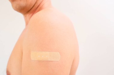 Aşı ya da enjeksiyondan sonra küçük bir bandajla bir adamın üst kolu. Sağlık, aşı ve tıbbi tedavi kavramı.