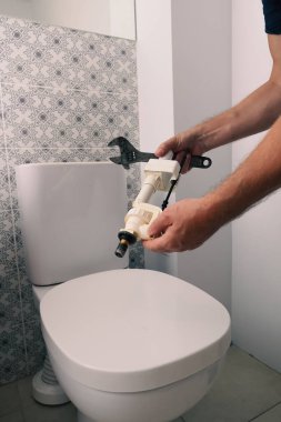 Sarnıçta çalışırken tuvalet doldurma vanası ve ingiliz anahtarı tutan becerikli bir elin yakın çekimi. Ev bakımı ve tesisat onarım servisi.