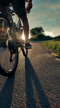 Gün batımında kırsal bir yolda pedal çeviren bir bisikletlinin alçak açılı yakın çekimi. Özgürlüğün sembolü, macera, fitness, sağlıklı yaşam tarzı ve açık hava aktivitesi..