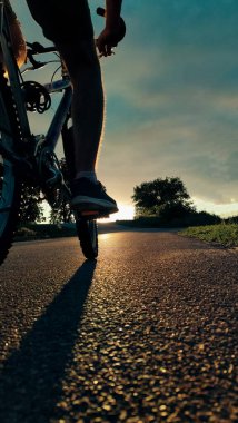 Gün batımında kırsal bir yolda pedal çeviren bir bisikletlinin alçak açılı yakın çekimi. Özgürlüğün sembolü, macera, fitness, sağlıklı yaşam tarzı ve açık hava aktivitesi..