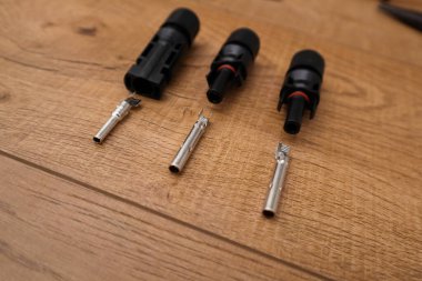 Güneş paneli kablolarını bağlamak için gerekli olan siyah plastik cisimleri ve metal pin ve soket lenslerini gösteren birçok parçalanmış MC4 konnektörünün yukarıdan görünüşü, açık tahta arka planlar ve ahşap bir yüzey üzerindeki metal temaslar üzerine yerleştirilir..