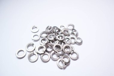 Bir grup ayrık kilit temizleyicisinin yüksek açılı görüntüsü. Metalik endüstriyel bağlayıcılar, beyaz bir yüzeye saçılmış cıvata ve vidaların gevşemesini önlemek için..