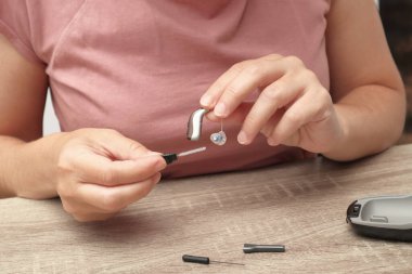 Daha iyi performans ve hijyen sağlamak için kulak arkası işitme cihazı olarak özel bir temizlik fırçası kullanan bir kişinin ellerinin yakın çekimi.