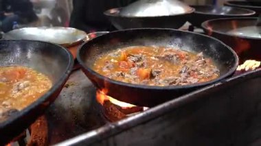 Aşçılık Sahnesi Domates tabanlı bir et yahnisi ile iki siyah tava, açık ateşte karahi, sokak yemeği