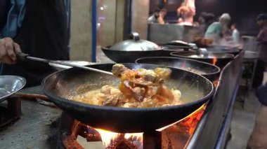 Alevler et ve sosla dolu büyük tavaları yalıyor. Karahi, hareketli açık hava yemekleri, sokak yemekleri.