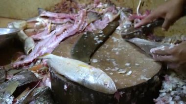 Bıçak ahşap bir blokta duruyor. Yanında tek bir balık var. Etrafı dağınık balık parçalarıyla çevrili.