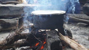 Açık ahşap ateşin üzerinde ısıtılan büyük siyah bir tencerenin yakın çekimi, yemek pişirme konsepti..