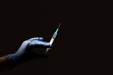 Siyah arka planda mavi eldivenli bir el enjeksiyon için sıvı içeren plastik bir şırınga tutar. Sağlık hizmeti, tedavi kavramı.