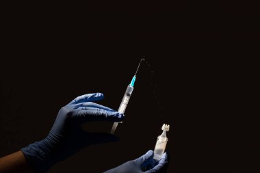 Siyah bir arka planda tıbbi eldivenli bir tıp çalışanının elinde ilaç spreyi olan bir şırınga. Ellerinde şırınga ve ilaç ampulü var..