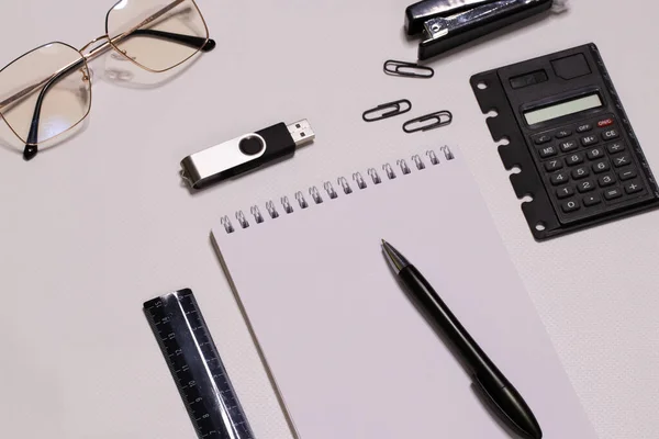 White desktop. Office supplies. Office, desk. On the table are glasses, a notebook, a pen, a ruler, a flash drive, and a calculator. Flat lay.