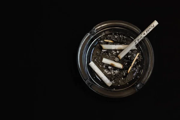 Un cenicero lleno de colillas de cigarrillos en primer plano sobre un fondo negro. — Foto de Stock