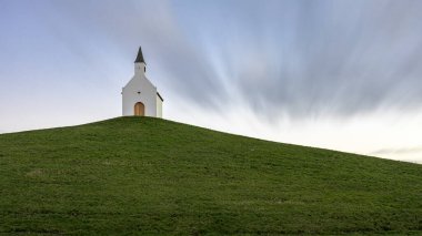 Çimenli bir tepenin üstünde küçük beyaz bir kilise. Parçalı bulutlu bir günde uzun bir çekim..