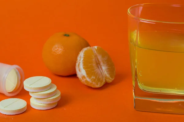 Vitamins tablets in water in a glass with citrus flavor on an orange background in a close-up