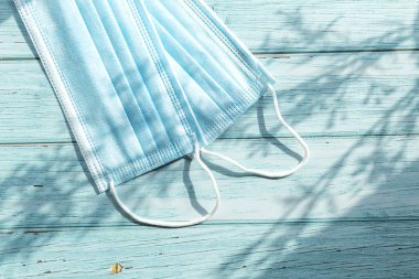 Ahşap bir arka planda tıbbi maske. Yukarıdan yakından bakınca, bir dalın gölgesiyle.