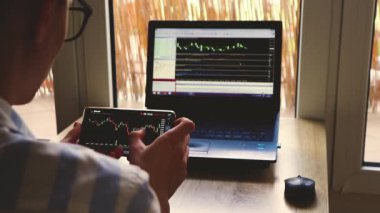 Adam telefondaki döviz çizelgesine yakından bakıyor, pencerenin arka planına karşı.