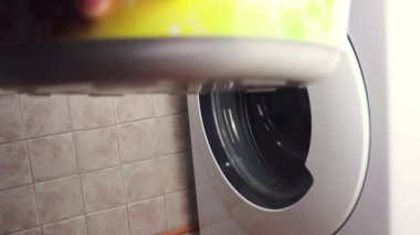 Sabahlıklı adam çamaşır makinesine çamaşır yıkamak için elbise yüklüyor.