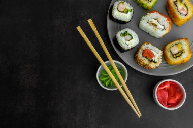 Gri bir tabakta suşi, arka planda koyu bir üst manzara, zencefil ve wasabi ile.