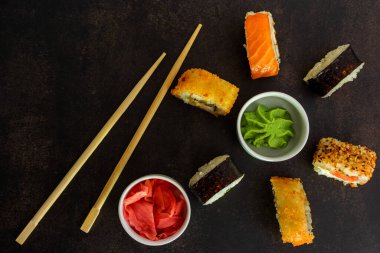 Koyu arkaplanda farklı seçeneklerden oluşan suşi. Yuvarlak görünüm için çubuklar. Wasabi ve zencefilli.