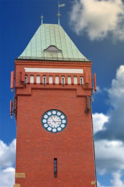 Mavi gökyüzüne karşı kocaman bir saati olan tuğla bir kuleye yakın çekim