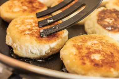 Yakın plan Ukrayna peynirli kekleri plastik çatalla sıkılmış tavada kızartılır.