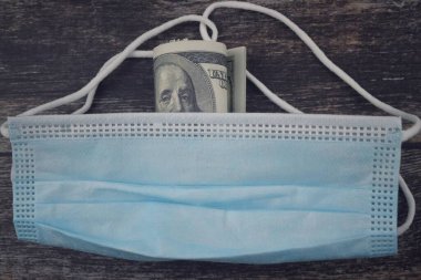 Ahşap arka planda yüz maskesi ve banknot resmi. Seçici odak resmi. Ekonomi ve sağlık kavramı.