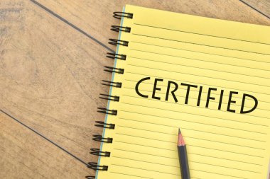 Kalem ve kitabın seçici odak resmi. Ahşap arka planda CERTIFIED yazıları var. İş konsepti