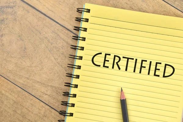 Kalem ve kitabın seçici odak resmi. Ahşap arka planda CERTIFIED yazıları var. İş konsepti